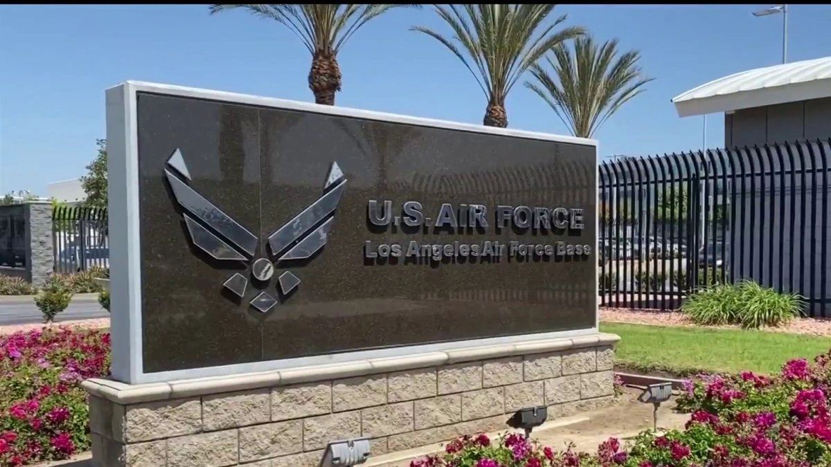 The granite entrance monument at Los Angeles Air Force Base carrying the United States Air Force emblem, palms and perimeter fencing behind it.