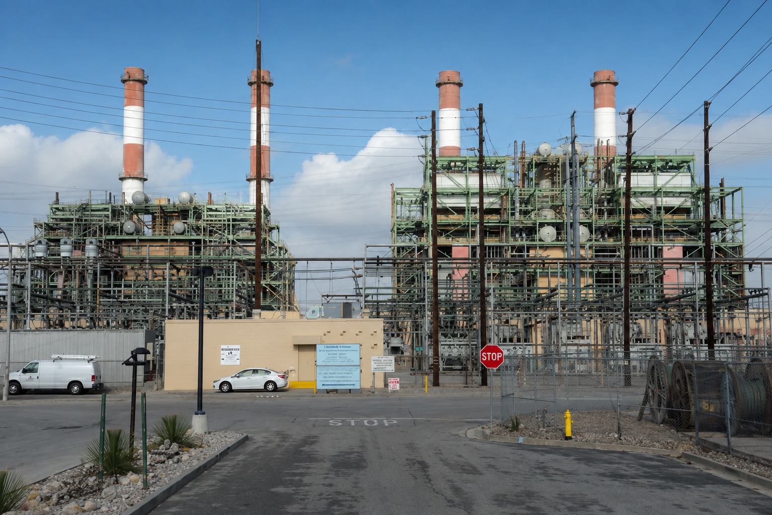The LADWP Valley Generating Station seen from its gate, two banked generating units in green steelwork under four banded stacks, switchyard structures across the frontage.