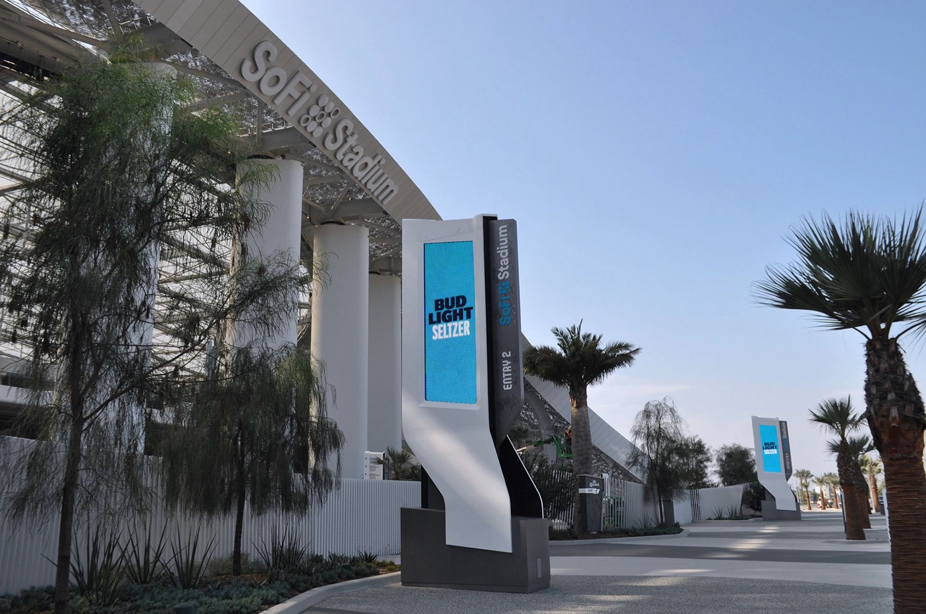 Two illuminated entry pylons at SoFi Stadium carrying digital display panels, the stadium roof canopy and lettering behind them.